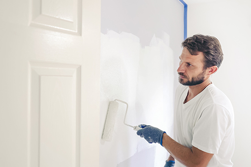 Man Using Roller Brush To Paint House Instead of Hiring House Painters Servicing East Tampa FL